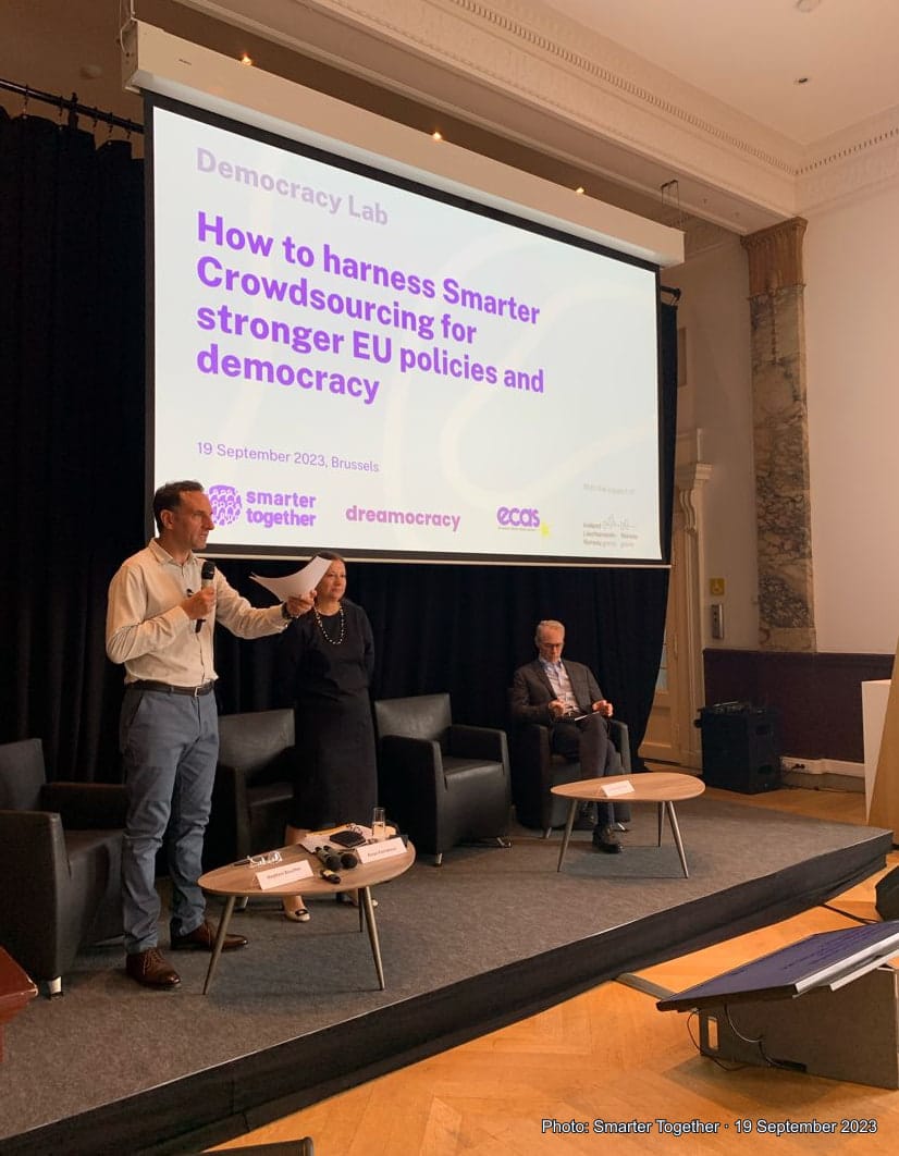 Portrait photograph of the Brussels Democracy Lab stage, with three people below the screen reading “How to harness Smarter Crowdsourcing for stronger EU policies and democracy” and “19 September 2023, Brussels”; Smarter Together photo credit at bottom.