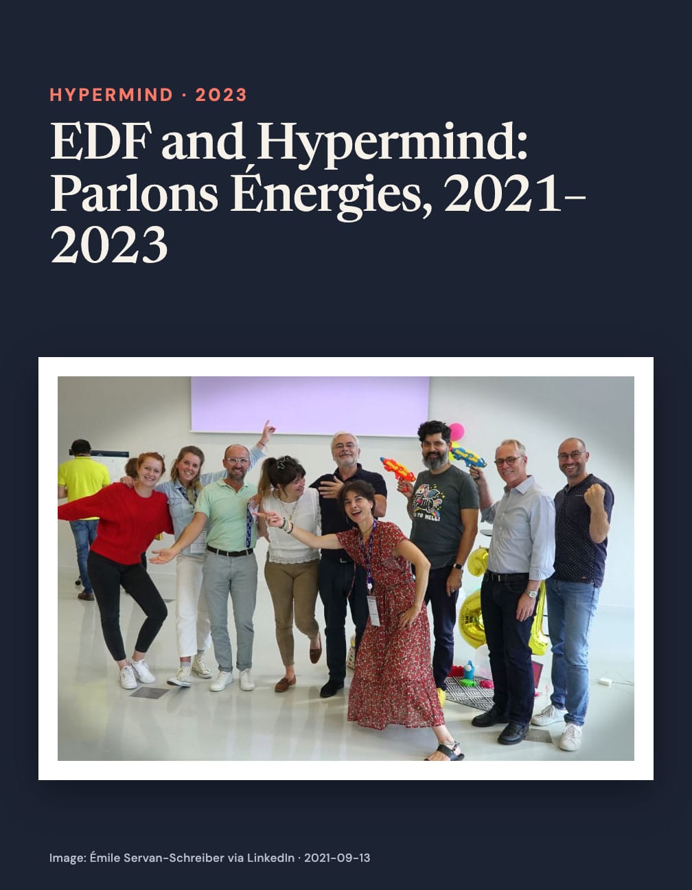 Navy card headed “EDF and Hypermind: Parlons Énergies, 2021–2023” above a group photo of smiling adults posing with balloons and colorful toy water pistols.
