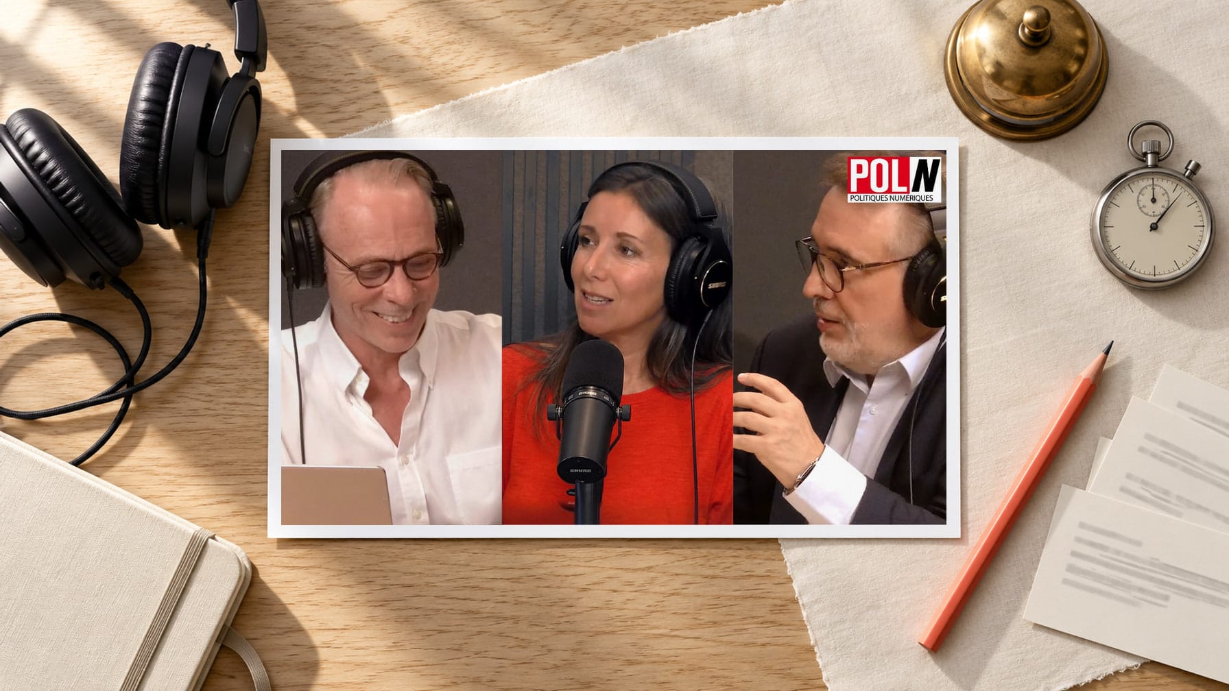 Editorial illustration of a printed still from the POL/N episode, showing Émile Servan-Schreiber, Delphine Sabattier and Bernard Benhamou at studio microphones, laid on a sunlit oak desk beside headphones, a brass desk bell, a stopwatch and a coral pencil.