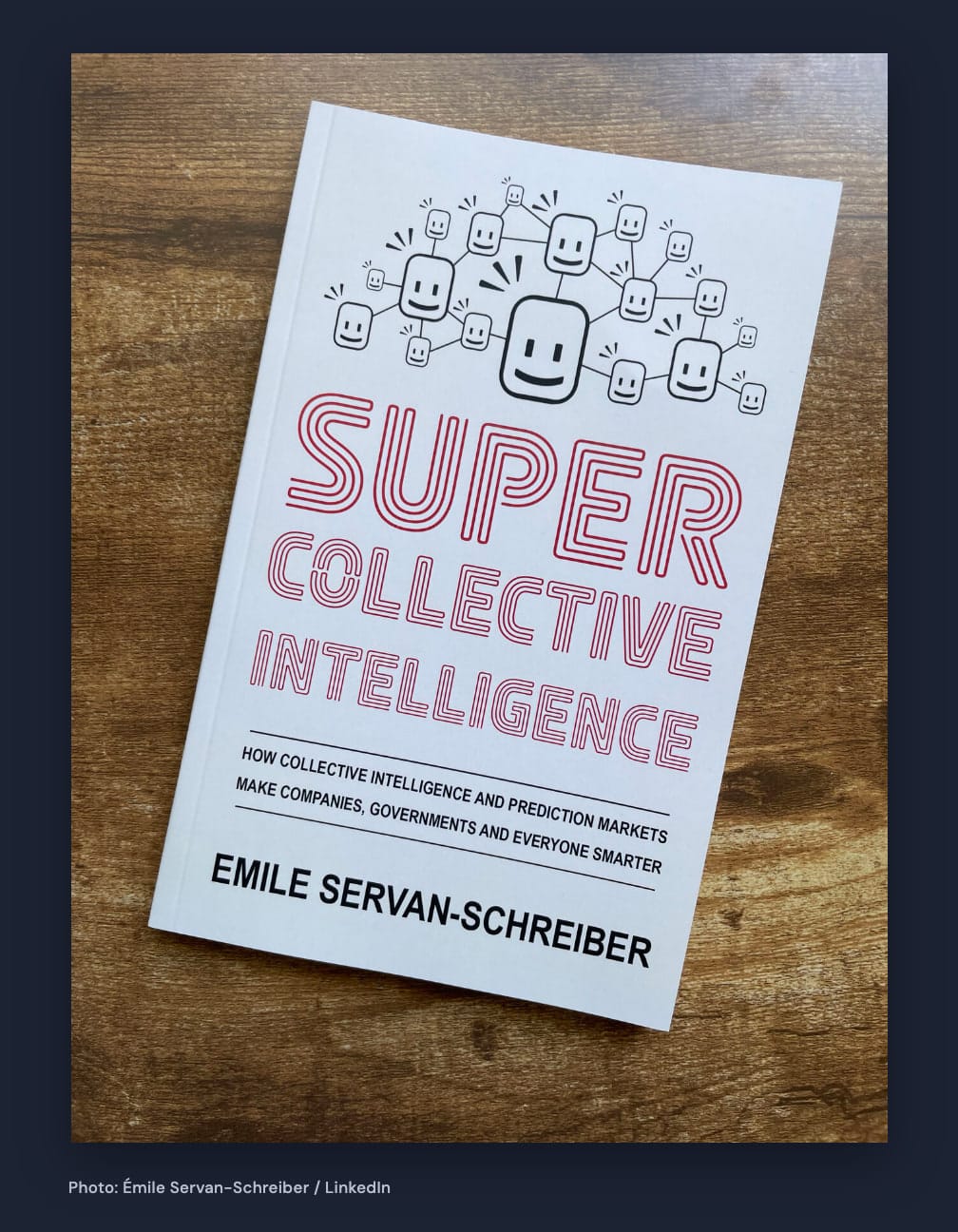 Photograph of the complete white Supercollective Intelligence paperback, with red title lettering and connected smiling faces, on a wooden surface with navy margins.